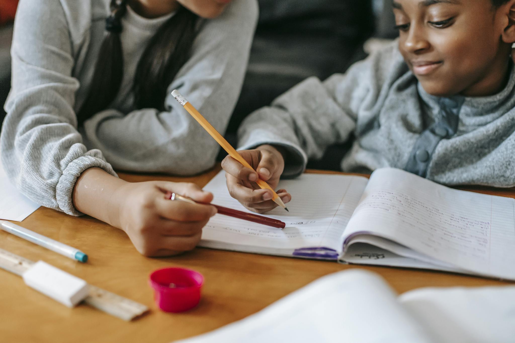 Two kids study together, focused on homework with pencils and notebooks, learning indoors.